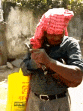 a man wearing a red head scarf is standing in front of a yellow container that says ' aa ' on it