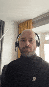a bald man wearing headphones and a karrimor shirt looks at the camera