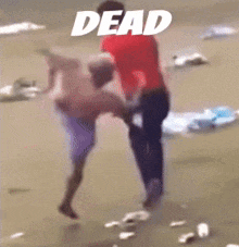 a man in a red shirt is holding another man in his arms while standing on a beach with the word dead above them .