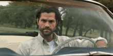 a man with a beard is sitting in a car with his arm resting on the steering wheel