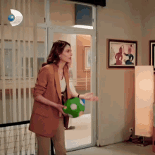 a woman in a brown jacket is holding a green soccer ball in her hand .