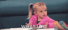 a little girl in a pink jacket is sitting at a table and saying what i do .