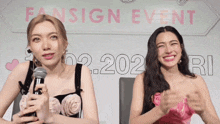 two women sitting in front of a sign that says fan sign event