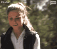 a woman wearing a black vest and a white shirt is smiling and looking at the camera .