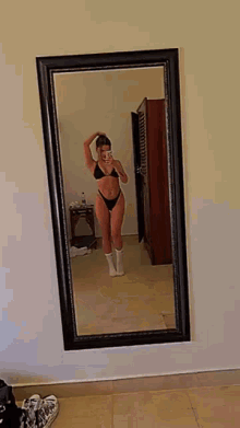 a woman in a bikini is taking a selfie in front of a full length mirror .