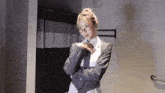 a woman in a suit and glasses stands in a bathroom