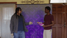 a man holding a bag of skittles talks to another man in front of a purple backdrop
