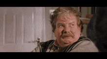 an older man with a mustache is sitting in front of a door .
