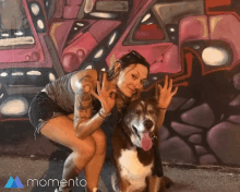 a woman kneeling down next to a dog in front of a wall that says momento on it