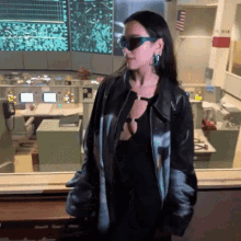 a woman wearing sunglasses and a black jacket stands in an office