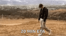 a man is walking across a dirt field with the words `` 20 min eta '' written on the bottom .