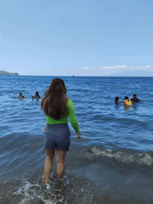 a woman in a green shirt and blue shorts is standing in the ocean