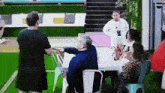 a group of people are sitting around a table with a woman standing behind them