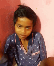 a young boy in a blue shirt with stars on it is sitting in front of a pink wall .
