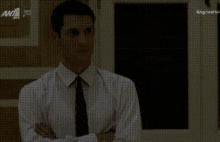 a man in a white shirt and black tie stands with his arms crossed in front of a sign that says ant on it
