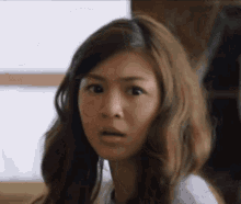 a woman with long hair is making a surprised face and looking at the camera .