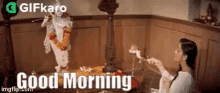 a woman is lighting a candle in front of a statue of krishna and saying `` good morning '' .