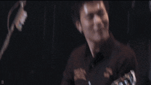a man is playing a guitar in a dark room and smiling .