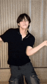 a young man in a black shirt and black pants is dancing in a room .