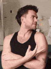 a man in a black tank top is sitting with his arms crossed .