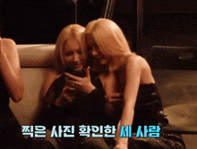 two blonde women are sitting next to each other on a couch looking at their cell phones