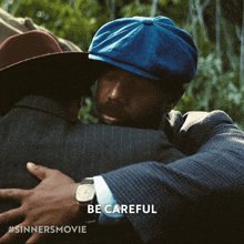 a man wearing a blue hat is hugging another man with the words be careful above him