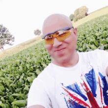 a man wearing sunglasses and a british flag t-shirt takes a selfie in a field