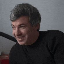 a man in a black sweater is smiling and looking at the camera