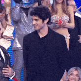 a man in a black suit stands in front of a crowd