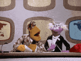 two muppets sitting at a desk with a red telephone in front of them