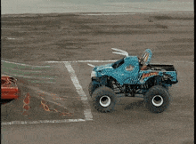 a blue monster truck is driving down a dirt road next to a red truck