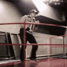 a man is standing on a railing holding a microphone and dancing .
