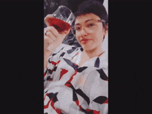 a woman wearing glasses holds a glass of red wine in her hand