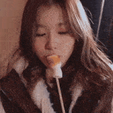 a woman is eating a marshmallow on a stick .
