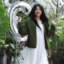 a woman in a white dress is standing in front of a large silver balloon that says c.