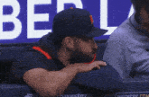 a man wearing a hat with the letter m on it sits in a dugout