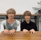 two young men are sitting at a table with their hands on the table