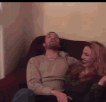 a man and woman are sitting on a couch laughing .