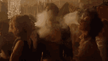 a group of people are smoking hookahs and blowing smoke into the air .