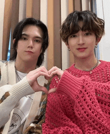 two young men in pink sweaters are making a heart with their hands