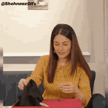 a woman in a yellow polka dot shirt is sitting on a couch opening a box