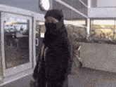 a man wearing a hooded jacket and a scarf is walking in front of a building .