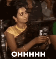 a woman in a sari is sitting in a crowd holding a cup of coffee and a can of beer .