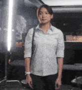 a woman wearing a white shirt and black pants stands in a dark room
