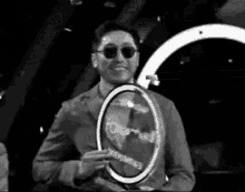 a man wearing sunglasses and a suit is holding a trophy in a black and white photo .