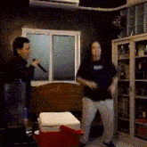a man is singing into a microphone while another man stands next to a red cooler