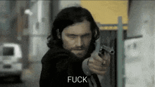 a man with long hair is pointing a gun at the camera and the word fuck is on the bottom