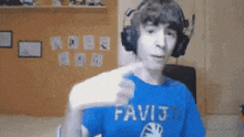 a man wearing headphones and a blue shirt with the word favij on it is holding a remote control .