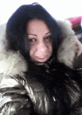a woman with long black hair is wearing a silver jacket with a white fur hood