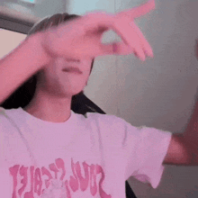 a man in a pink shirt is covering his face with his hand .